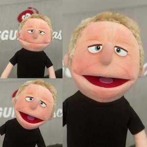 Może przedstawiać: Ręcznie wykonana kukiełka z ludzką twarzą, o jasnej skórze, blond włosach i niebieskich oczach. Kukiełka ma czerwone usta i nosi czarną koszulkę. Projekt kukiełki jest szczegółowy, z widocznymi szwami.