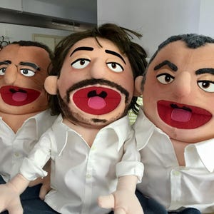 May include: Three handmade puppet heads with expressive features. Each puppet has a large, open mouth with a red interior, and is wearing a white collared shirt. The puppets have different hair and facial hair styles, and are designed to resemble people.