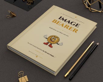 Può includere: Un diario devozionale color crema intitolato "Image Bearer" con un personaggio a fumetti a forma di moneta sulla copertina. Il diario ha dettagli dorati, con matite e fermagli.