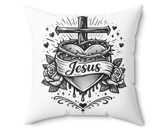 Può includere: Cuscino quadrato bianco con un design grafico in bianco e nero. Il design include un cuore, una croce, una corona di spine, rose e la parola "Jesus" su uno striscione. Elementi decorativi come cuori e raggi completano il design.