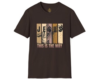 Può includere: T-shirt marrone con un design grafico che mostra la parola "JESUS" e una croce. Sotto, il testo recita "THIS IS THE WAY". Il design utilizza colori beige, marrone e beige.