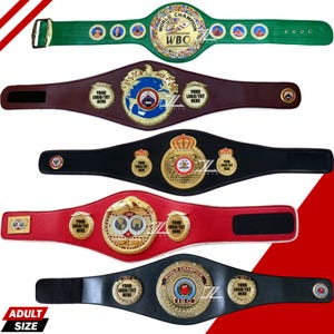 Puede incluir: Una variedad de cinturones de campeonato para adultos en varios colores, incluyendo verde, marrón, negro y rojo. Cada cinturón presenta un gran emblema central adornado con detalles dorados y el texto "WBO" o "IBO". Los cinturones tienen cierres ajustables y espacios para logotipos personalizados.