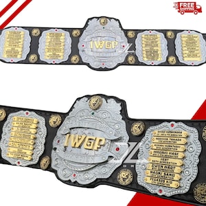 May include: Two professional wrestling championship belts. The belts are black with silver and gold accents. The center plate reads "IWGP HEAVYWEIGHT CHAMPION". The side plates list names. The belts are decorated with lion head emblems.