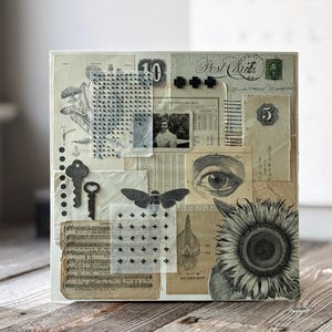 Könnte beinhalten: Gemischte Medien-Collage auf quadratischer Leinwand. Das Kunstwerk zeigt Vintage-Ephemera, darunter botanische Illustrationen, Notenblätter und eine Postkarte. Dekorative Elemente sind Schlüssel, ein Schmetterling und eine Sonnenblume. Die Farbpalette ist überwiegend neutral mit Sepia-Tönen.