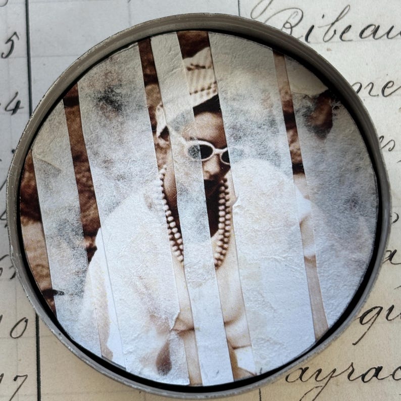 May include: A circular metal container featuring a sepia-toned image of a person wearing sunglasses and a pearl necklace. The image is divided by vertical white strips. The background includes handwritten script.