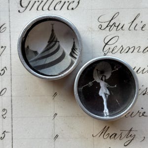 May include: A pair of vintage silver cufflinks. One shows a black and white image of a circus tent, the other a performer. The background is a handwritten ledger with the word "Grillieres".