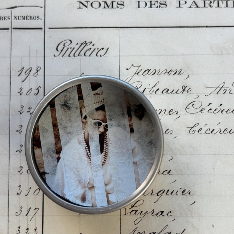 May include: A circular magnifying glass with a silver frame, displaying a vintage photograph. The image features a person wearing sunglasses and a pearl necklace. The background is an aged ledger with handwritten script.