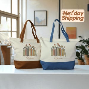 May include: Two canvas tote bags. One has a brown base and handles, the other has a blue base and handles. Both bags are off-white with a floral and book design, and the name "Maria" printed below.
