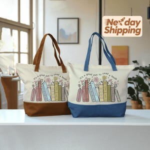 May include: Two canvas tote bags with the text "It's a good day to read a book." One bag has a brown base and handles, the other has a blue base and handles. Both bags feature a floral and book design.