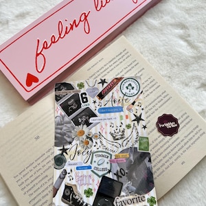 Può includere: Una scatola rettangolare rosa con le parole "feeling lucky" in corsivo rosso e un collage di immagini e testo su una pagina di libro. Il collage include foto, disegni e testo, tra cui le parole "Joey" e "favorite person".