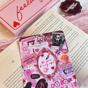 May include: A pink box with the words "feeling lucky" in red script, a sticker, and a decorative card with a pink Ghostface design and the text "Do you like scary movies?" on a book.