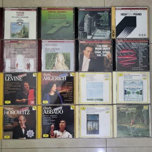 May include: A collection of classical music CDs featuring various composers and performers. The CDs have colorful covers with text and images, including portraits and artwork. The collection includes works by Mozart, Vivaldi, and Schubert.