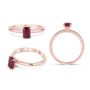 May include: Rose gold ring with a rectangular, deep red gemstone. The ring is displayed from various perspectives, showcasing the band and the gemstone's setting. The design is simple and elegant, suitable for everyday wear or special occasions.