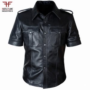Puede incluir: Una camisa negra de manga corta con cuello en punta, charreteras en los hombros y dos bolsillos en el pecho con solapas abotonadas. El cierre frontal consta de botones de presión metálicos. El logo Hustle Flame Industries aparece arriba a la izquierda.
