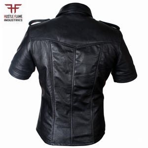 May include: A black short-sleeved leather shirt featuring a collar, shoulder epaulets, and vertical seam detailing on the back. The top left corner displays the logo and text Hustle Flame Industries in red and black.