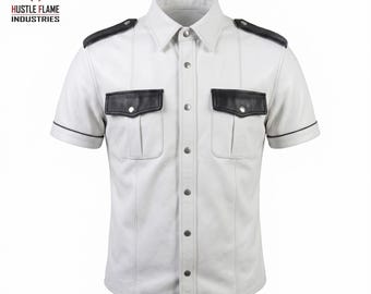 May include: A white short-sleeve shirt featuring black shoulder epaulets, black pocket flaps, and black trim on the sleeves. The shirt has a button-down front with silver-toned metal snaps and includes the text Hustle Flame Industries.
