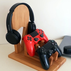 K&ouml;nnte beinhalten: Ein Gaming-St&auml;nder aus hellem Holz mit einem schwarzen Philips-Kopfh&ouml;rer, einem roten Controller und einem schwarzen Controller. Der St&auml;nder hat ein schlichtes Design. Im Hintergrund ist ein Laptop zu sehen.