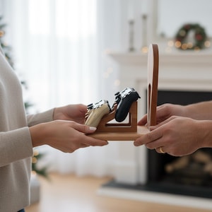 K&ouml;nnte beinhalten: Ein Holzst&auml;nder f&uuml;r Gamecontroller mit zwei Controllern, einem schwarzen und einem beigen. Der St&auml;nder wird von zwei Personen gehalten. Der St&auml;nder ist aus hellbraunem Holz gefertigt und hat ein schlichtes, modernes Design.