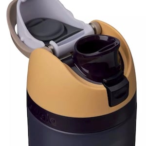 Puede incluir: Primer plano de una botella de agua con tapa abatible. La botella es principalmente azul marino con un acento beige y negro. La tapa est&aacute; abierta, revelando una boquilla para beber de color p&uacute;rpura oscuro y un interior blanco y gris.