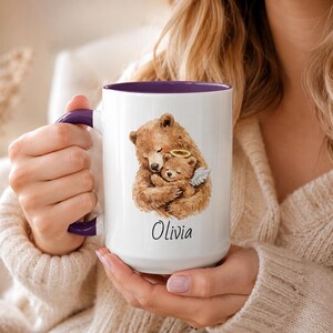 Purple handle remembrance mug held in two hands, featuring watercolor bear and angel baby bear artwork with personalized name Olivia on a white ceramic mug.