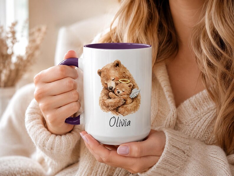 Purple handle remembrance mug held in two hands, featuring watercolor bear and angel baby bear artwork with personalized name Olivia on a white ceramic mug.