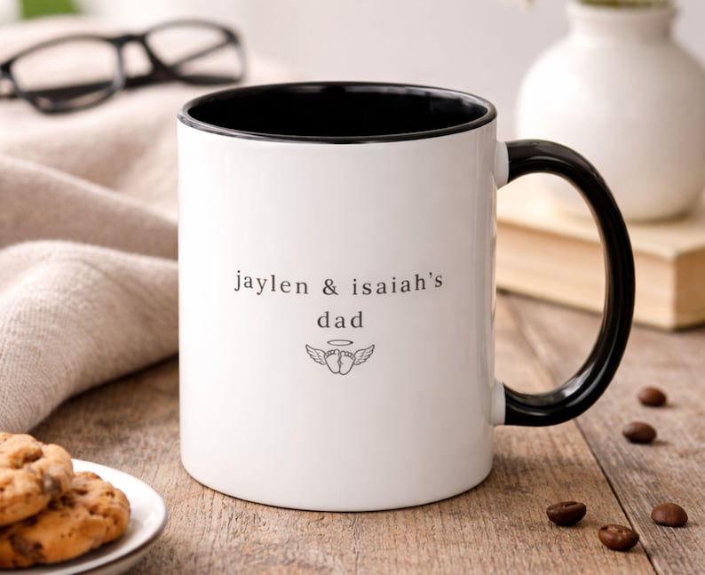 Personalized bereaved dad mug with black handle and interior, baby names and angel baby feet design on white ceramic coffee cup on rustic wood table.