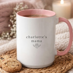 Personalized remembrance mug with pink handle and rim, ‘charlotte’s mama’ text and small angel wing icon, styled on woven coaster with cookies and cozy knit blanket background