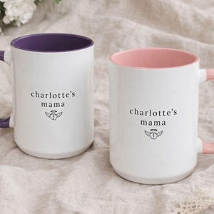Set of two personalized loss mom mugs, white ceramic with purple and pink handles and colored interiors, ‘charlotte’s mama’ design, resting on neutral linen bedding for a soft comfort gift look.