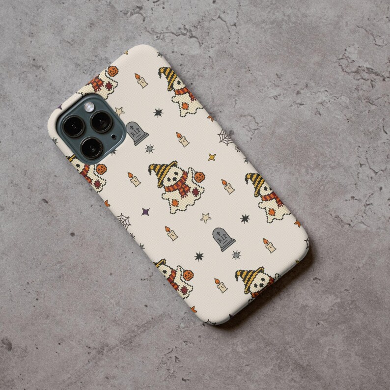 Smartphone protective case mockup printed with retro needlework halloween ghost pattern on a gray concrete surface.