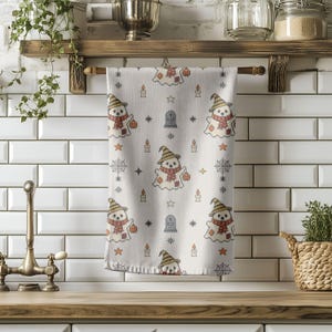 Kitchen hand towel mockup printed with embroidered ghost and spiderweb pattern hanging in a cozy rustic interior.