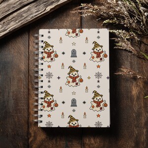 Spiral notebook mockup displaying patchwork ghost pattern on cover, placed on vintage wooden background with dried plants.