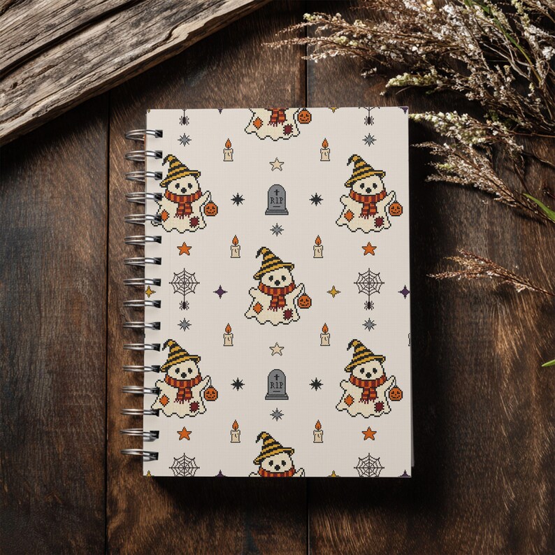Spiral notebook mockup displaying patchwork ghost pattern on cover, placed on vintage wooden background with dried plants.