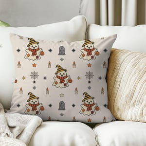 Decorative throw pillow mockup featuring cross-stitch ghost and stars illustration on a sofa for cozy autumn home decor.