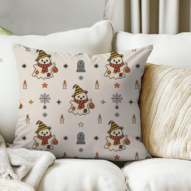 Decorative throw pillow mockup featuring cross-stitch ghost and stars illustration on a sofa for cozy autumn home decor.