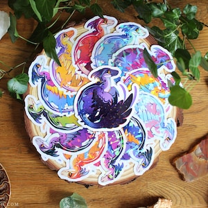 Peut inclure: Une collection d'autocollants circulaires représentant des dinosaures raptors stylisés dans diverses couleurs vives, notamment violet, orange, bleu et rose. Chaque autocollant présente une finition holographique, avec un raptor violet foncé au centre.