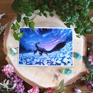 Könnte beinhalten: Ein rechteckiger Kunstdruck, der ein dunkles, gefiedertes, dinosaurierartiges Wesen zeigt, das in einem Feld aus weißen Blumen unter einem leuchtend blauen Nachthimmel voller Sternschnuppen und einem kosmischen Nebel steht.