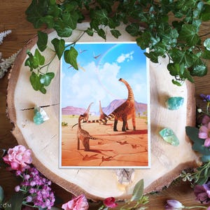 Pode incluir: Uma impressão de arte retangular apresentando uma paisagem pré-histórica com três dinossauros saurópodes de pescoço longo caminhando sobre um solo desértico rachado em tons de laranja sob um céu azul claro com nuvens e um arco-íris.