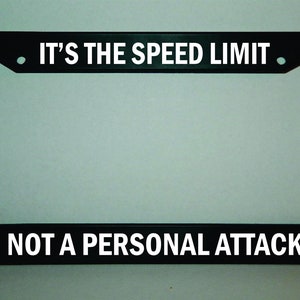 May include: Black license plate frame with white text that reads "IT'S THE SPEED LIMIT. NOT A PERSONAL ATTACK."