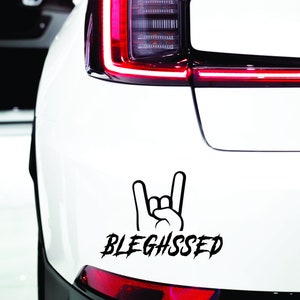 May include: A white car with a black decal of a hand making the rock and roll sign with the word "BLEGHSSSED" underneath.