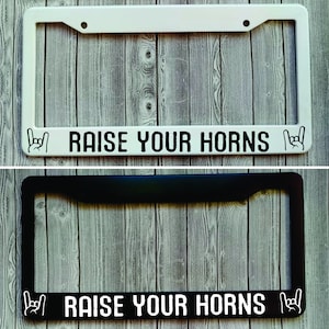 May include: Two license plate frames, one white and one black, with the text "RAISE YOUR HORNS" and a rock and roll hand gesture on each side.