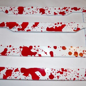 May include: Two white license plate frames with a red splatter paint design.