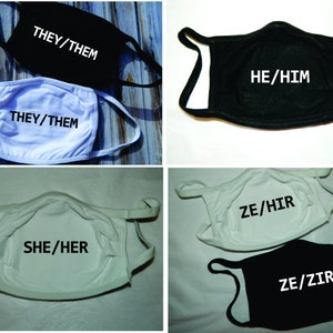 May include: Four cloth face masks with different pronoun combinations printed on them. The masks are white and black. The pronouns are "THEY/THEM", "HE/HIM", "SHE/HER", and "ZE/HIR" and "ZE/ZIR".