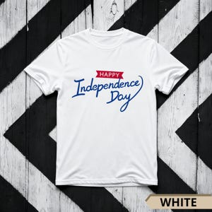 Può includere: T-shirt bianca con la scritta "Happy Independence Day" in blu, con uno striscione rosso sopra la parola "Independence". La maglietta è esposta su una superficie di legno a strisce bianche e nere.