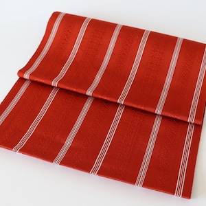 May include: Red fabric with white stripes. The fabric has a textured surface.