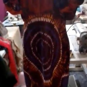 May include: A long tie-dye dress in shades of brown, purple, and white. The dress has a circular pattern on the front and a flowing silhouette. The sleeves are short and the fabric appears lightweight.