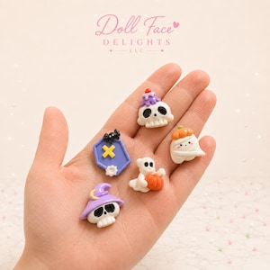 May include: Five small, colorful resin cabochons featuring Halloween-themed designs: a skull with a purple candle, a purple coffin with a black spider and yellow cross, a white ghost with a pumpkin, a white mummy with a pumpkin, and a skull with a purple hat.