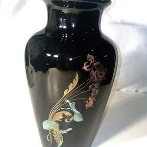 May include: Black ceramic vase with a gold rim and floral design. The vase features a glossy finish and a decorative pattern of stylized flowers and leaves in shades of gold, teal, and purple.