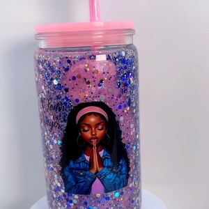 May include: A clear tumbler with a pink lid and straw, filled with purple glitter. The tumbler features an illustration of a woman with the text "Lean on Prayer".