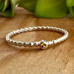 May include: A silver beaded bracelet with a single, round, amber-colored gemstone in the center.
