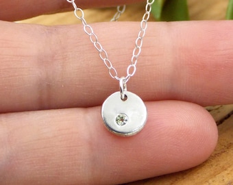 May include: A silver chain necklace with a small round pendant featuring a single clear gemstone.